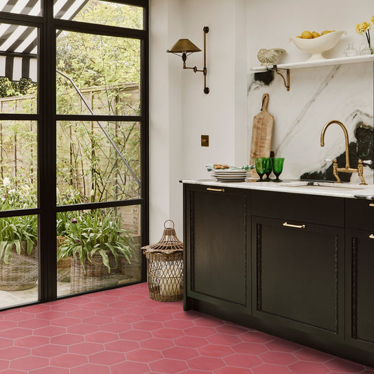 Modern kitchen with black cabinets, red hexagonal tiles, and a view of greenery outside.